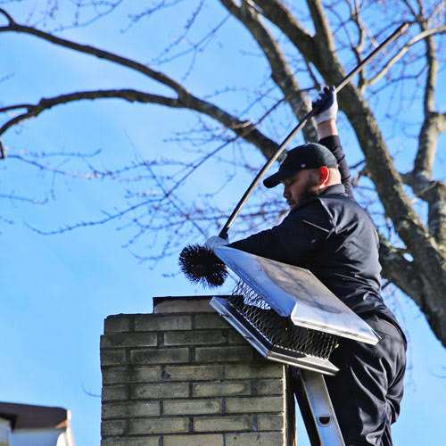 Chimney sweep working beside a metal chimney cap