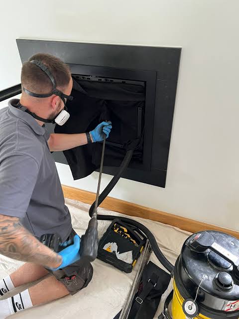 Technician cleaning a modern black firebox with vacuum equipment