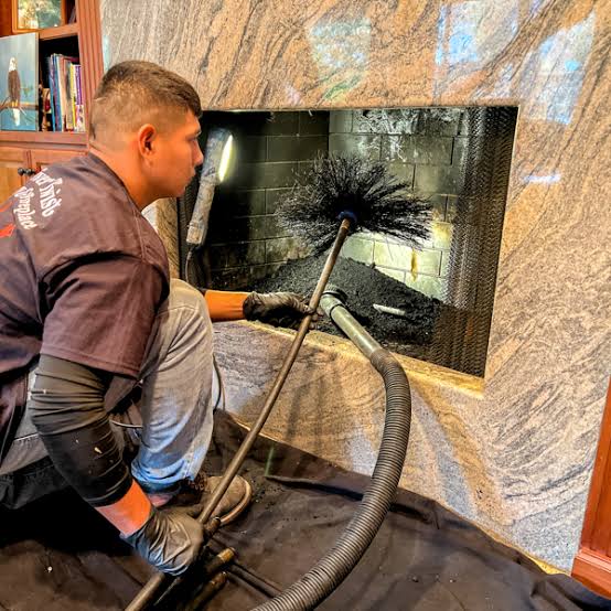 Chimney sweep brushing the inside of a stone fireplace