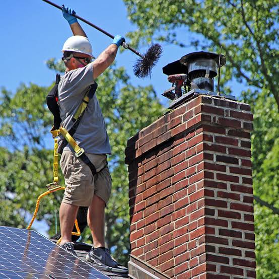 Chimney sweep using a long brush on a brick rooftop chimney