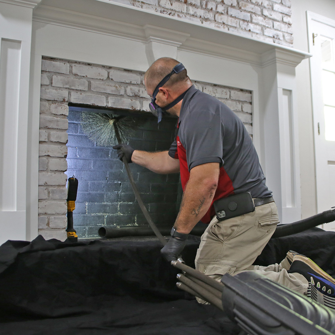 Chimney professional cleaning the firebox of a white brick fireplace